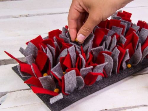 Håndholdt fodersøgematte til gnavere, lavet af blødt filt i rød og grå, der stimulerer dyrets naturlige instinkter og gør fodring sjov. Ideel til både hamstere og marsvin.